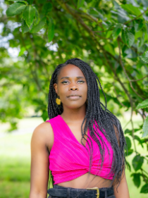 headshot of poet Vanessa Kisuule, a black woman with long braids wearing a bright pink top. She is standing outside in front of a tree and looking straight at the camera.